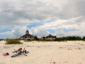 a view of the port boca grande lighthouse museum from the beach, with a bicycle and towel in the foreground